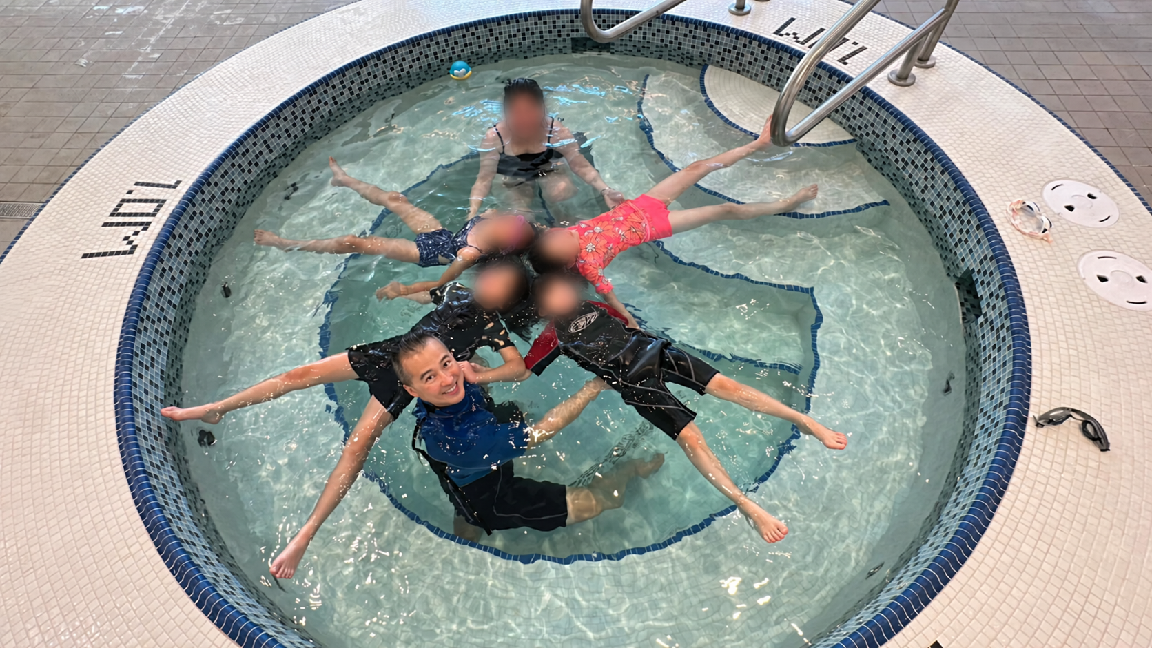 Coach Jo smiling while helping several children practise floating in a circle; their faces are blurred